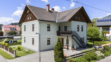 Freistehendes Haus mit heller Fassade, Satteldach und einem Balkon mit Außentreppe in ländlicher Umgebung.