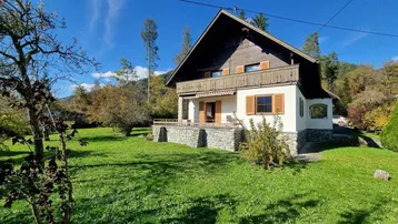 Traditionelles Haus mit Holzbalkon und großem Garten unter blauem Himmel.