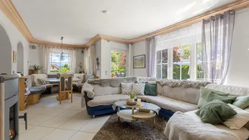 Helles Wohn- und Esszimmer mit Fliesenboden, Kaminofen und großen Fenstern zum Garten.