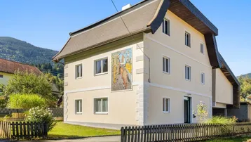 Traditionelles Haus mit heller Fassade und dekorativem Mosaik in ländlicher Umgebung.