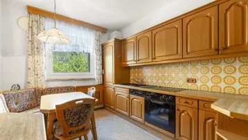 Wohnküche mit Holzschränken, Essbereich und gemusterten Fliesen als Spritzschutz.