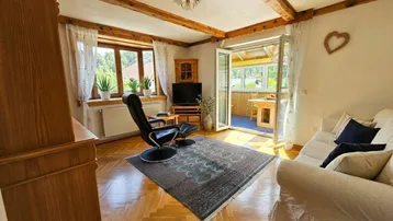 Helles Wohnzimmer mit Holzbalken, Parkettboden und Zugang zu einem Wintergarten.