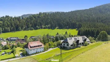 Luftaufnahme eines ländlichen Anwesens mit mehreren Gebäuden, umgeben von grünen Wiesen und Wäldern.