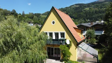 Gelbes Haus mit rotem Ziegeldach, Balkon und Blick auf die umliegende Berglandschaft.
