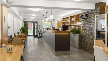 Moderner Restaurantbereich mit stilvoller Bar, Holztischen und einer markanten Steinwand als Akzent.