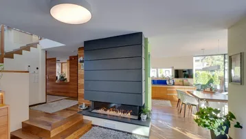 Offener Wohn- und Essbereich mit modernem Kamin, Holzboden und Treppe zum Obergeschoss.
