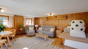 Gemütliches Wohnzimmer im alpinen Stil mit Holzvertäfelung, Kachelofen und bequemen Sitzmöbeln.