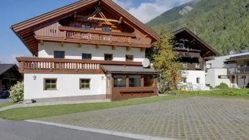 Traditionelles Alpenhaus mit Holzbalkonen und weißer Fassade vor bergiger Kulisse.