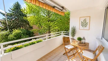 Heller Balkon mit Markise, Gartenmöbeln und Blick ins Grüne, ideal zum Entspannen im Freien.