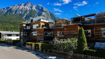 Moderne Holzfassaden-Gebäude mit Terrassen und Bergblick unter blauem Himmel.