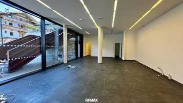 Geräumiger, leerer Gewerberaum mit großen Fenstern, Säule und modernen Deckenleuchten, ideal für verschiedene Nutzungen.