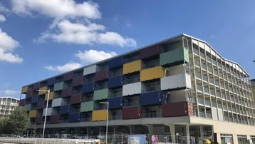 Modernes Wohngebäude mit farbigen Container-Elementen an der Fassade unter blauem Himmel.