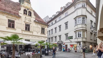 Belebte Gasse mit historischen Gebäuden, Außengastronomie und Passanten in der Stadt.