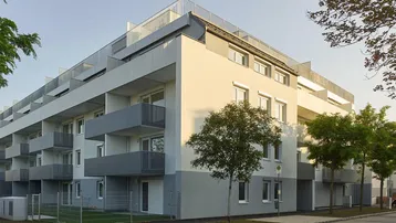 Moderne Wohnanlage mit weiß-grauer Fassade, zahlreichen Balkonen und Flachdach.