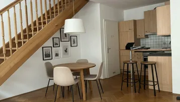 Offener Wohn-Essbereich mit Holzboden, Esstisch und integrierter Küchenzeile unter der Treppe.
