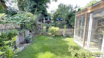 Gepflegter Gartenbereich mit Rasenfläche, verschiedenen Pflanzen und einem kleinen Gewächshaus.