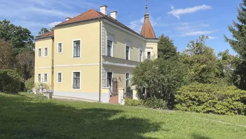 Historisches Gebäude mit gelber Fassade und rotem Ziegeldach, umgeben von einem weitläufigen Garten.