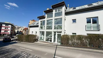 Moderne Gebäudefassade mit großer Glasfront und einem französischen Balkon an einem sonnigen Tag.
