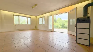Großes Wohnzimmer mit Terrakottafliesen, Kaminofen und Zugang zur Terrasse.