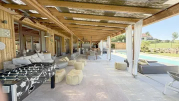 Große überdachte Terrasse mit Lounge-Möbeln, Esstisch und Tischfußball, ideal für Unterhaltung im Freien.