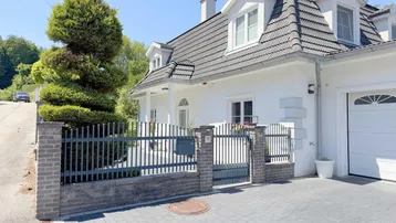 Weißes Einfamilienhaus mit dunklem Ziegeldach, Vorgarten und gepflasterter Einfahrt.