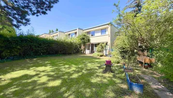 Großer, gepflegter Garten mit Rasenfläche und üppiger Bepflanzung hinter einem Reihenhaus.