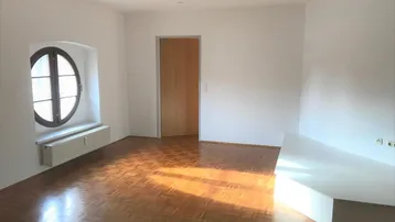 Helles Zimmer mit Fischgrätparkett, runden Fenstern und weiß gestrichenen Wänden.