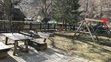 Großer Gartenbereich mit Spielplatz, Sandkasten und Sitzgelegenheiten, umgeben von Natur und Bergen.