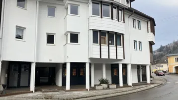 Mehrstöckiges Gebäude mit weißer Fassade und mehreren Fenstern, an einer Straße gelegen, mit Balkonen.