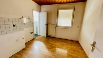 Leere Küche mit Holzdecke, Laminatboden und Fliesen an der Wand, bereit für eine neue Einrichtung.
