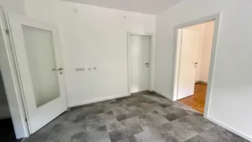 Leeres Zimmer mit weißen Wänden, modernem Vinylboden und mehreren Türen.