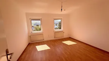 Helles Zimmer mit Parkettboden, zwei Fenstern und einem schönen Blick ins Grüne.