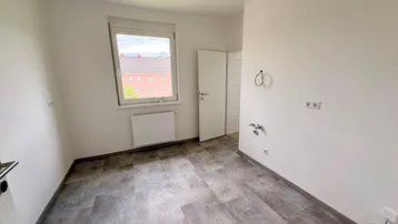 Leerer Raum mit grauem Vinylboden, Fenster und Anschlüssen für Haushaltsgeräte, ideal als Hauswirtschaftsraum.