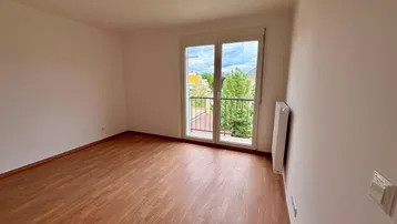 Heller Wohnraum mit Laminatboden, großem Fenster und Zugang zu einem französischen Balkon.