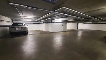 Tiefgarage mit einem geparkten Auto, sichtbaren Rohren an der Decke und Betonboden.