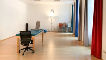 Geräumiger Büroraum oder Therapieraum mit hellem Holzfußboden und einfacher Einrichtung.