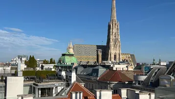 Panoramablick über die Dächer Wiens mit dem Stephansdom unter blauem Himmel.