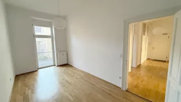 Helles Zimmer mit Holzboden und Zugang zu einem französischen Balkon, das viel Tageslicht bietet.