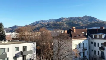 Panoramablick auf die umliegende Berglandschaft und die Dächer der Stadt unter blauem Himmel.
