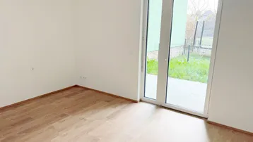 Helles Zimmer mit Laminatboden und direktem Zugang zu einer kleinen Terrasse und Gartenbereich.