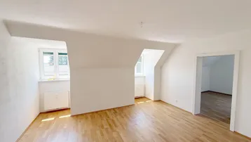 Helles, leeres Zimmer mit Dachschrägen und Parkettboden, ideal als Wohn- oder Schlafbereich.