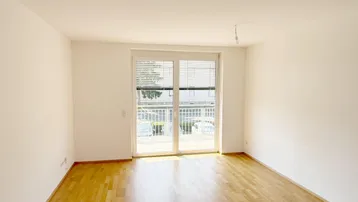 Helles Zimmer mit Parkettboden und Zugang zu einem Balkon, ideal als Wohn- oder Schlafbereich.