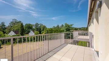 Geräumiger Balkon mit Fliesenboden und weitem Blick ins Grüne unter blauem Himmel.