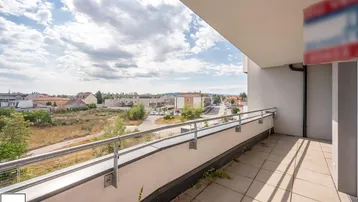 Geräumiger Balkon mit Fliesenboden und weitem Blick über die Umgebung unter einem bewölkten Himmel.