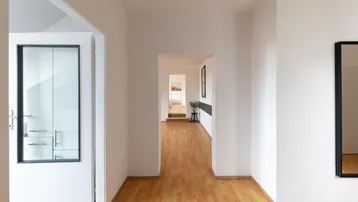 Heller Flur mit Holzfußboden und weiß gestrichenen Wänden, der zu weiteren Räumen führt.