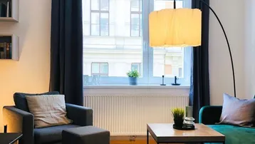 Helles Wohnzimmer mit modernem Sofa, Sessel, Holzboden und großer Bogenlampe.