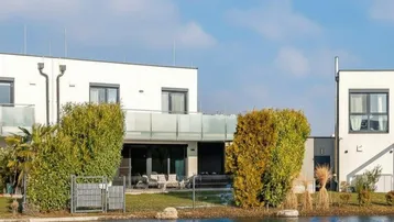 Moderne weiße Gebäude am Wasser mit gepflegter Gartenanlage und klarem Himmel.