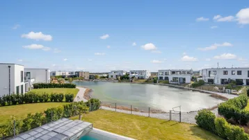 Weitläufiger Blick auf den See und die moderne Wohnsiedlung unter blauem Himmel.