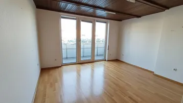 Heller, leerer Raum mit Parkettboden, Holzbalkendecke und Zugang zu einem Balkon.