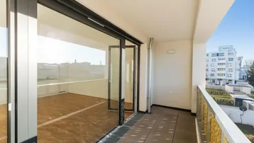 Geräumiger Balkon mit großen Glasschiebetüren und Blick auf die Umgebung.